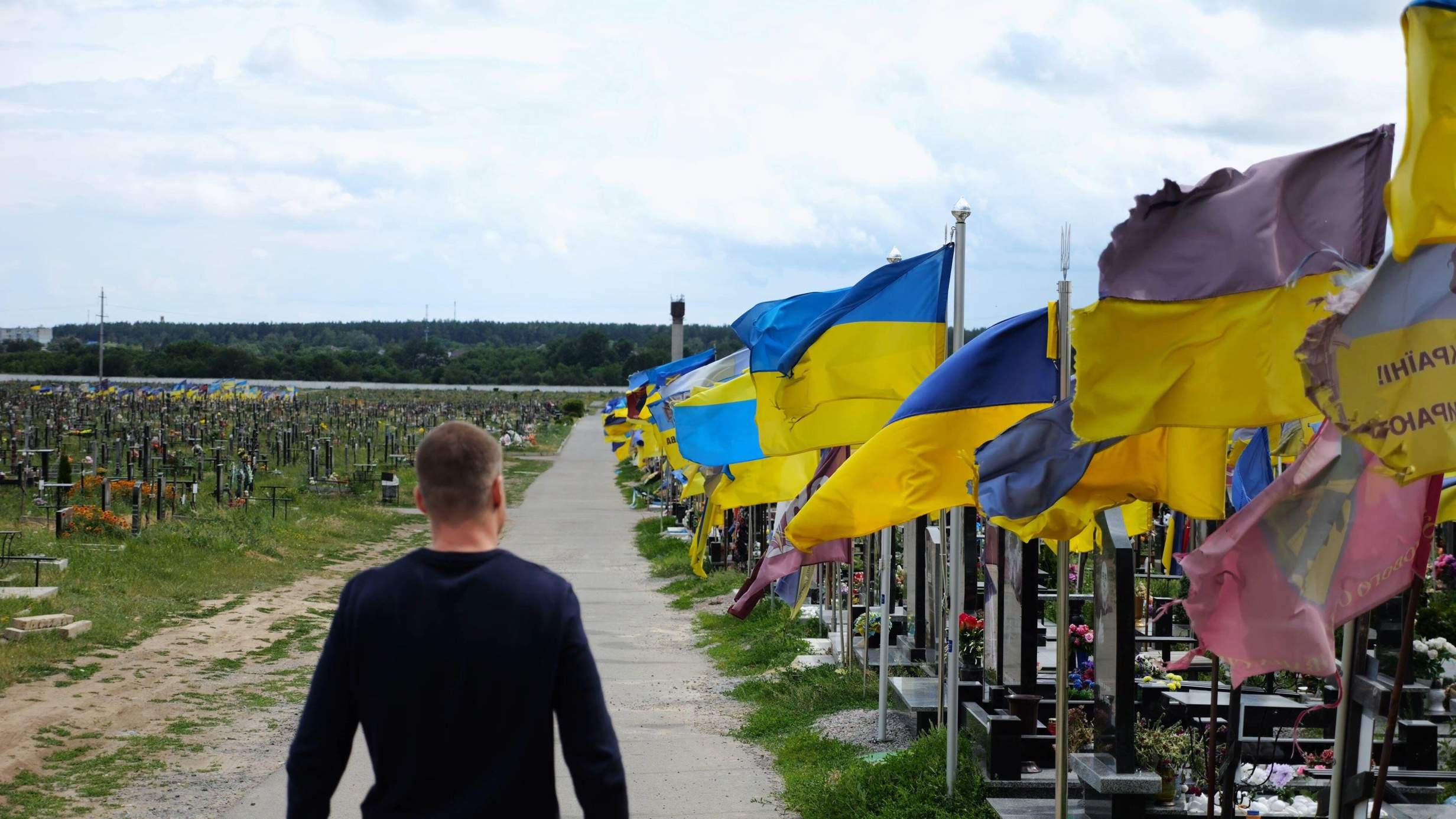 A man in mourning walks among countless graves of Ukrainian soldiers with national flags at the military cemetery in Kharkiv. Photo: Levgen Shcherbyna