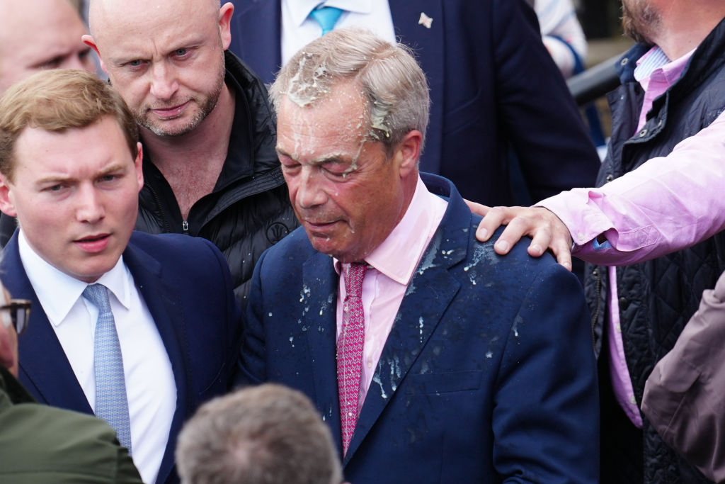 CLACTON-ON-SEA, ENGLAND - JUNE 4: George Cottrell (L) looks on as Reform UK party leader Nigel Farage reacts after a woman threw what appeared to be a milkshake over him, as he launches his election candidacy at Clacton Pier on June 4, 2024 in Clacton-on-Sea, England. The launch follows yesterday's announcement that Nigel Farage will stand as an MP in Clacton at the 4 July general election and takes over from Richard Tice as leader of Reform UK. The Conservative-held seat in Essex was the first to elect a UKIP MP in 2014, a party that Farage founded. (Photo by Carl Court/Getty Images)